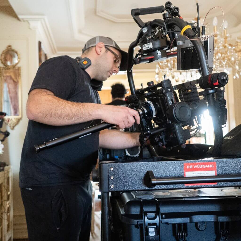 FX Productions Canada A man adjusts a professional video camera rig on set indoors for FX Productions Canada, wearing a headset and cap, with equipment and chandeliers visible in the background. Toronto Video Production Company