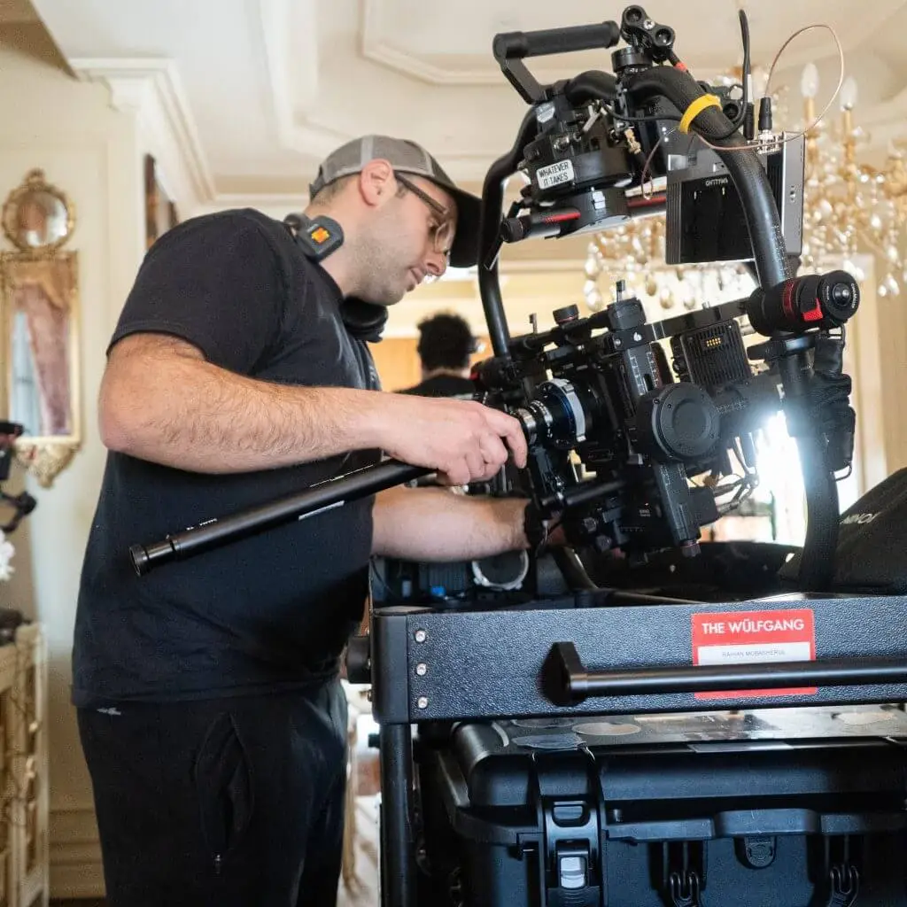FX Productions Canada A man adjusts a professional video camera rig on set indoors for FX Productions Canada, wearing a headset and cap, with equipment and chandeliers visible in the background. Toronto Video Production Company