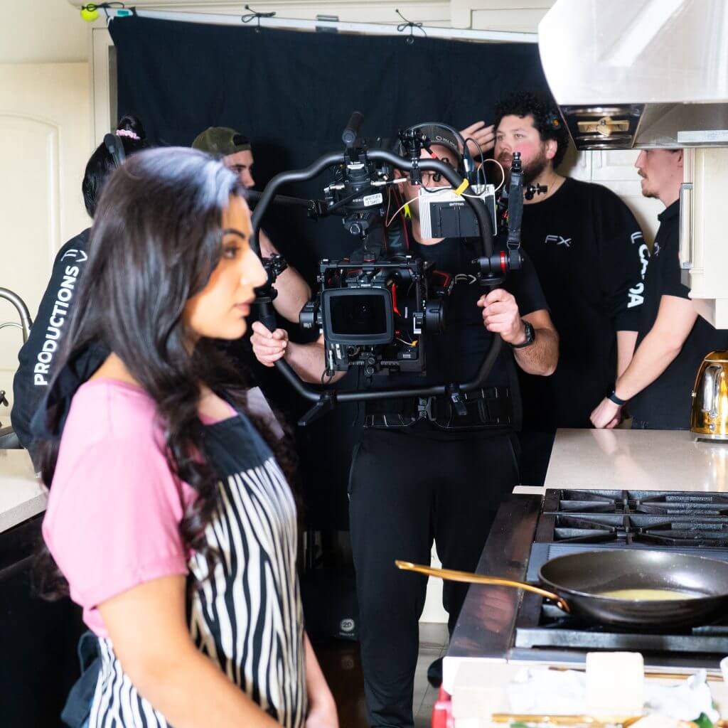 FX Productions Canada A film crew from FX Productions Canada records a woman in an apron standing by a stove in a kitchen, with cameras and equipment visible in the background. Toronto Video Production Company