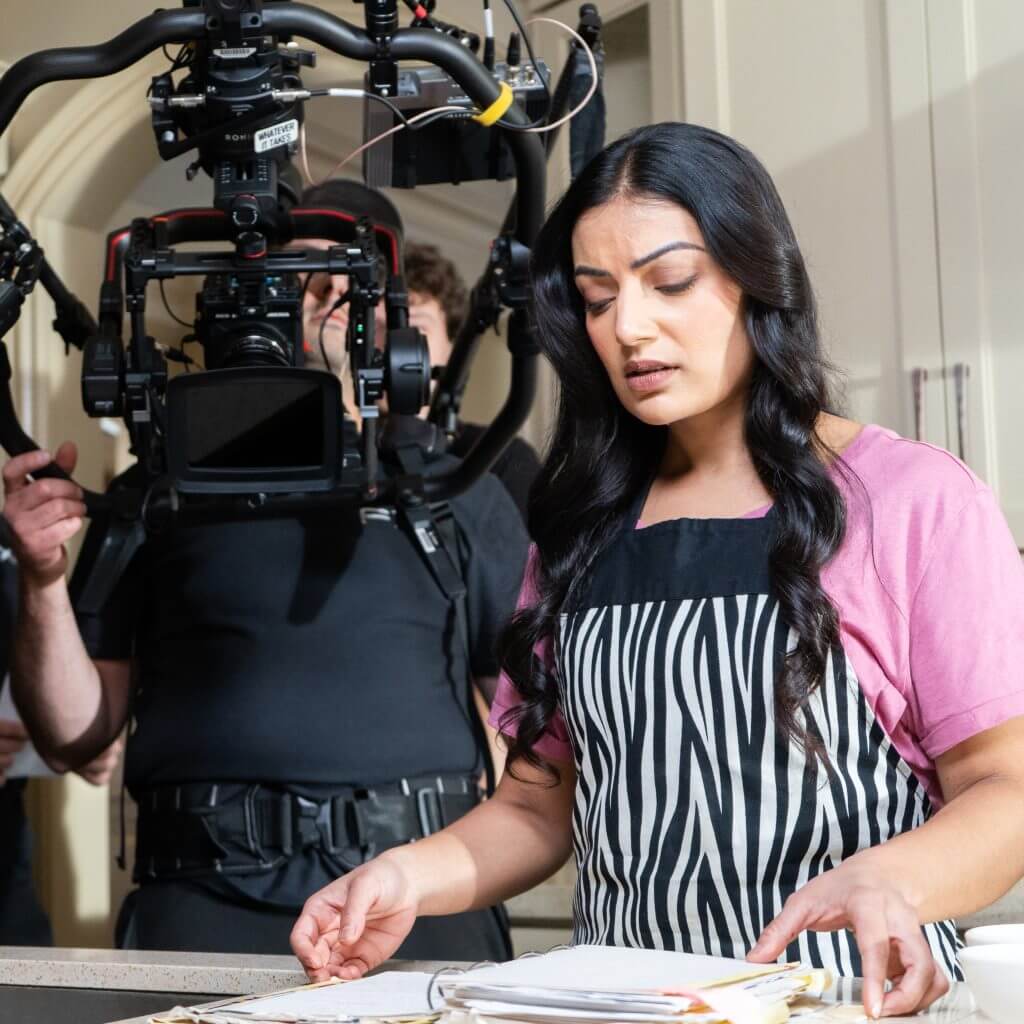 FX Productions Canada A woman wearing a striped apron stands at a counter with papers as a cameraman from FX Productions Canada films her using a large camera rig. Toronto Video Production Company