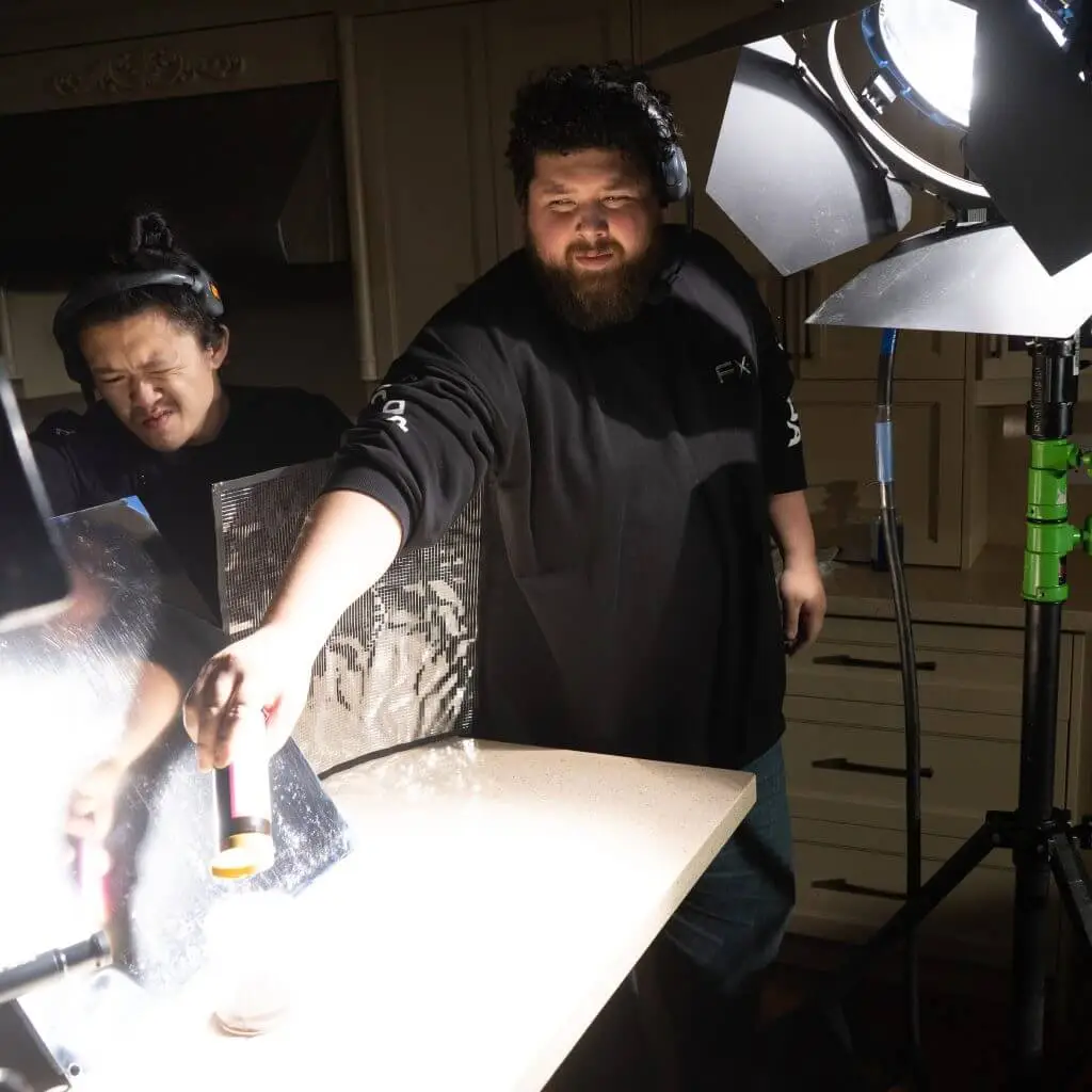 FX Productions Canada Two people from FX Productions Canada work on a food photography setup in a kitchen, adjusting lighting and holding a tool over a plate on the counter. Toronto Video Production Company