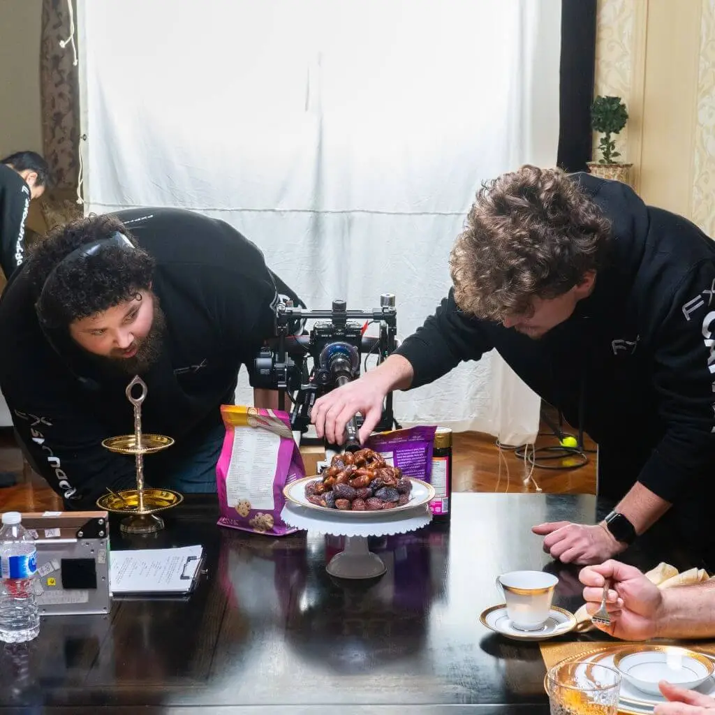 FX Productions Canada Two men from a Toronto Video Production company set up a camera to film or photograph a plate of dates on a cake stand, carefully adjusting the arrangement on a dining table set for tea. Toronto Video Production Company