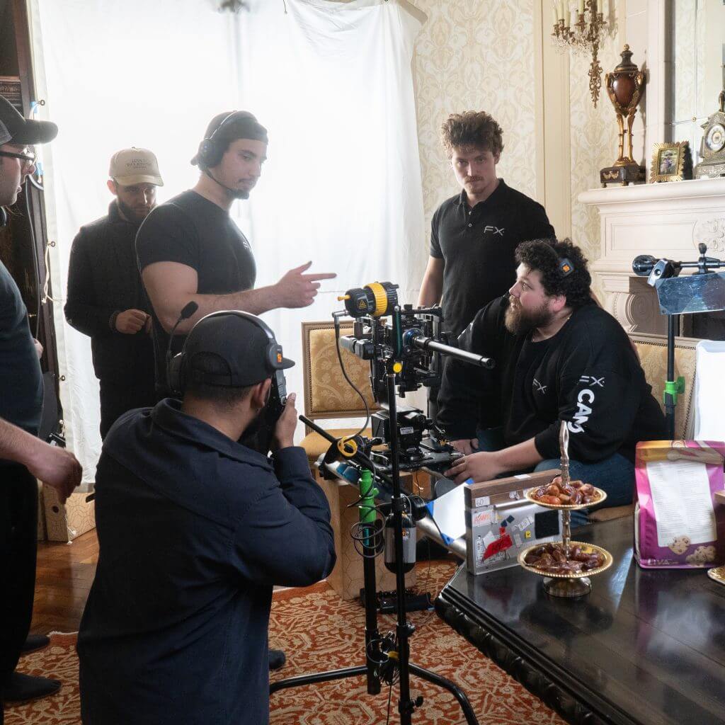 FX Productions Canada A film crew from FX Productions Canada sets up and discusses a shot indoors, with camera equipment and snacks visible on a table in the foreground. Toronto Video Production Company