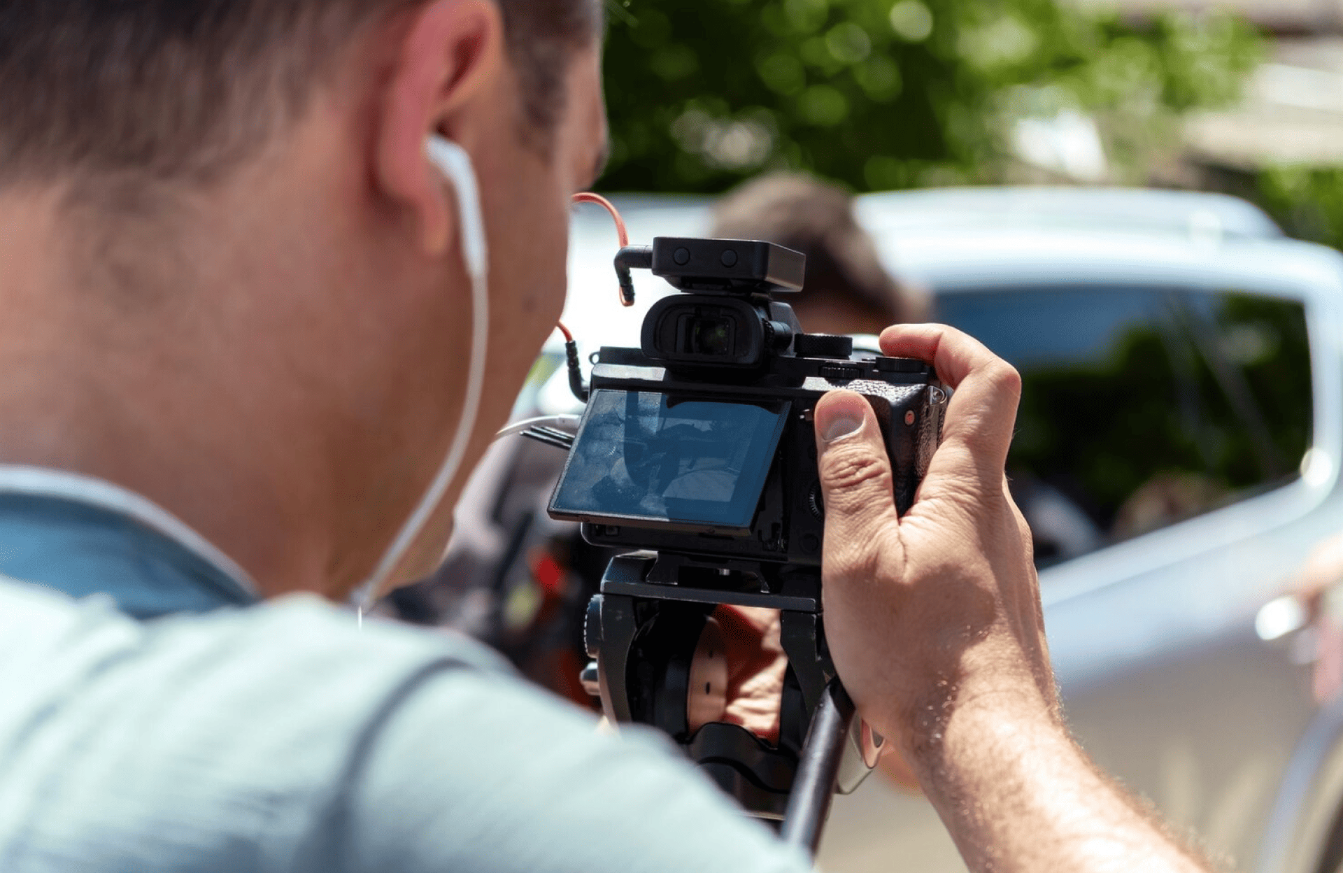 FX Productions Canada A person wearing earphones films with a handheld video camera outdoors, focusing on a car with an open window—a scene typical of a Toronto Production Company project. Toronto Video Production Company