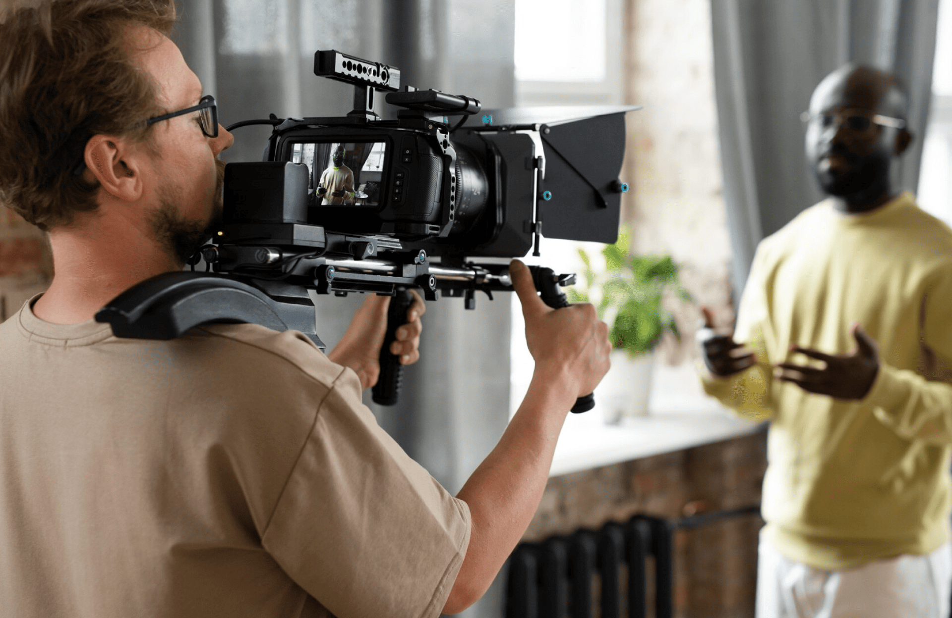 FX Productions Canada A person from FX Productions Canada operates a shoulder-mounted video camera, filming another person who is speaking and gesturing indoors near a window. Toronto Video Production Company