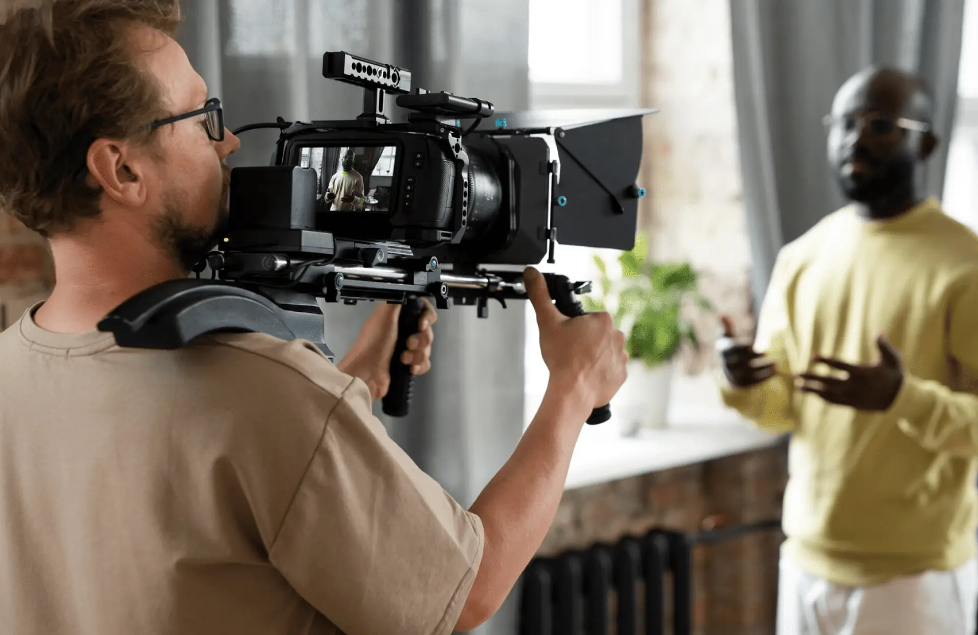 FX Productions Canada A person from FX Productions Canada operates a shoulder-mounted video camera, filming another person who is speaking and gesturing indoors near a window. Toronto Video Production Company