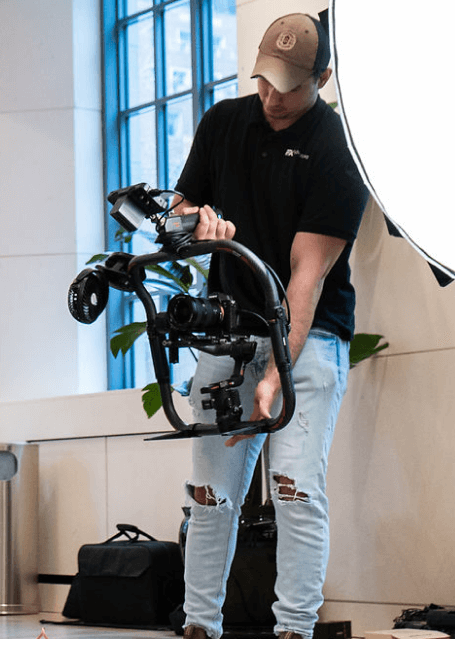 FX Productions Canada A person in a cap and ripped jeans operates a professional camera stabilizer rig indoors near a large window and light reflector, showcasing the creative process at FX Productions Canada, a leading Toronto Video Production company. Toronto Video Production Company