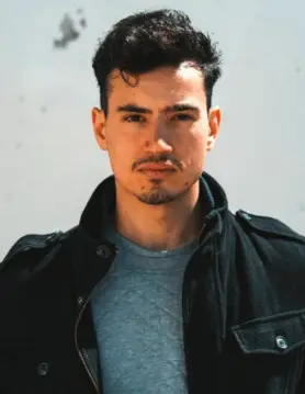 FX Productions Canada A man with short, dark hair and a trimmed beard wears a dark jacket over a gray shirt, standing against a light background—perfect for showcasing the talent behind Toronto Video Production. Toronto Video Production Company