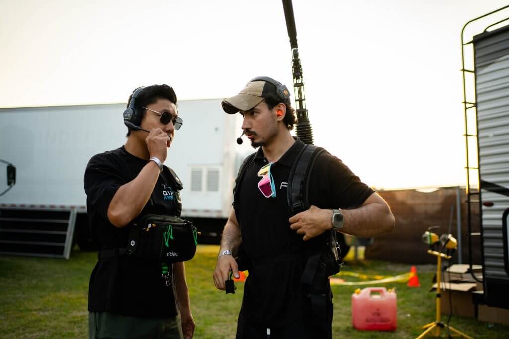 FX Productions Canada Two men wearing headsets and black shirts stand outdoors near trailers, communicating; one holds a boom microphone and the other adjusts his earpiece, showcasing behind-the-scenes work for a Toronto Video Production project. Toronto Video Production Company