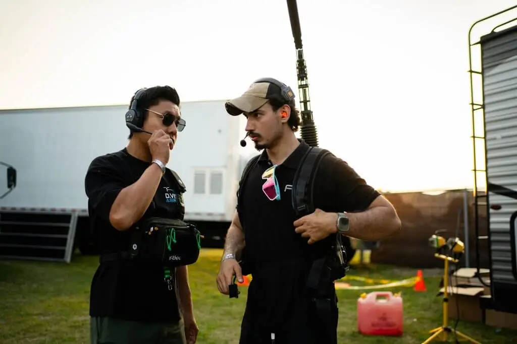 FX Productions Canada Two men wearing headsets and black shirts stand outdoors near trailers, communicating; one holds a boom microphone and the other adjusts his earpiece, showcasing behind-the-scenes work for a Toronto Video Production project. Toronto Video Production Company