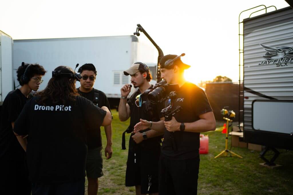 FX Productions Canada A group of five people wearing headsets and black clothing from FX Productions Canada discuss near film equipment outdoors at sunset, with one person holding a camera rig. Toronto Video Production Company