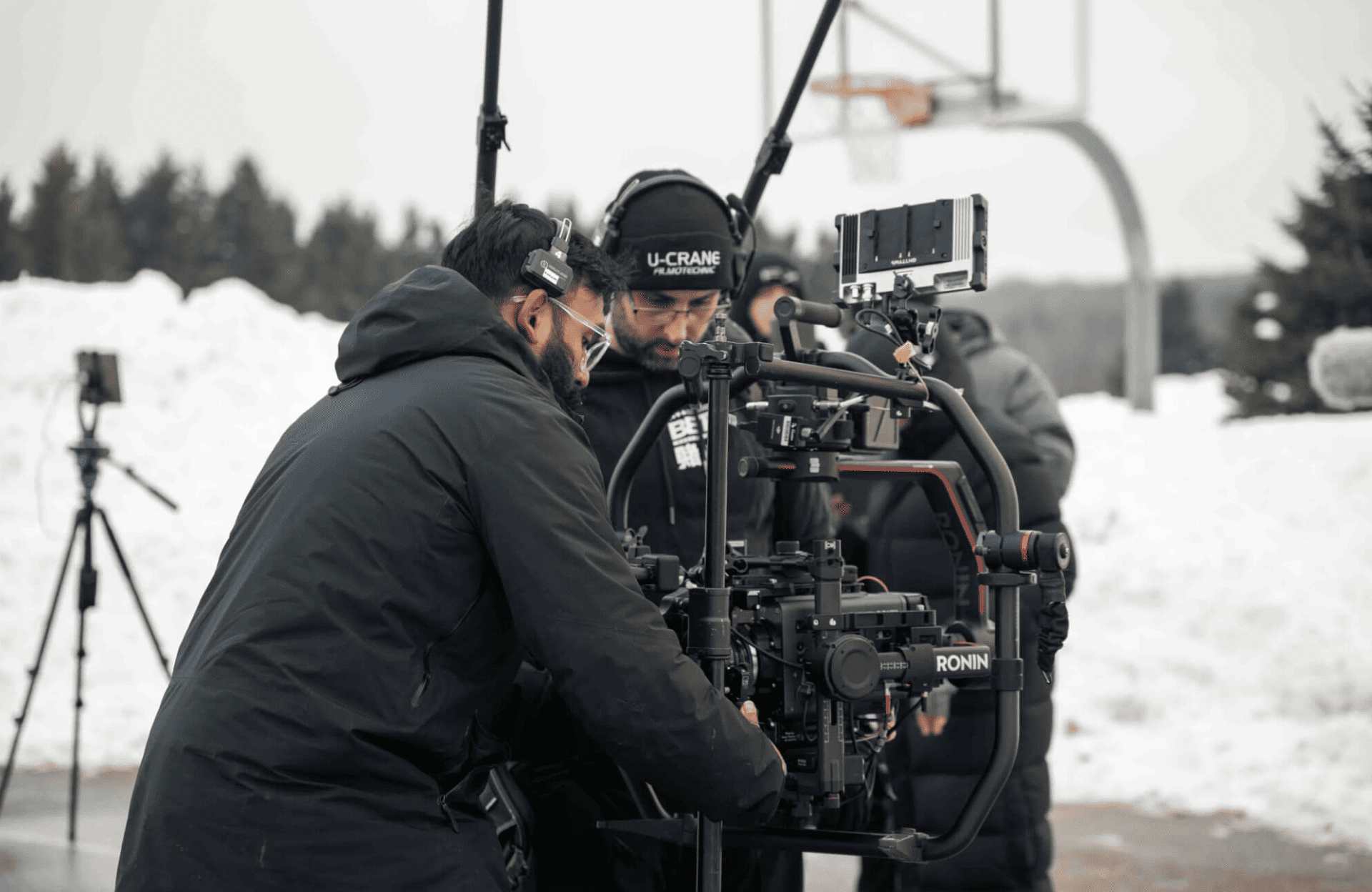 FX Productions Canada Two people adjust a professional camera rig outdoors in a snowy setting, with other filming equipment and a basketball hoop visible in the background—a typical scene for an FX Productions Canada Toronto Production Company shoot. Toronto Video Production Company