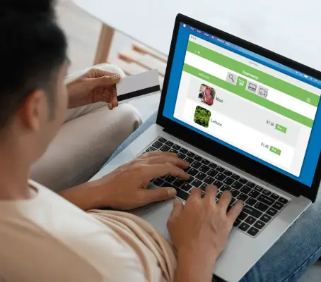 FX Productions Canada A person holds a credit card while shopping for vegetables online, browsing images and prices of mint and lettuce on their laptop. This scene is brought to life by Toronto Video Production experts. Toronto Video Production Company