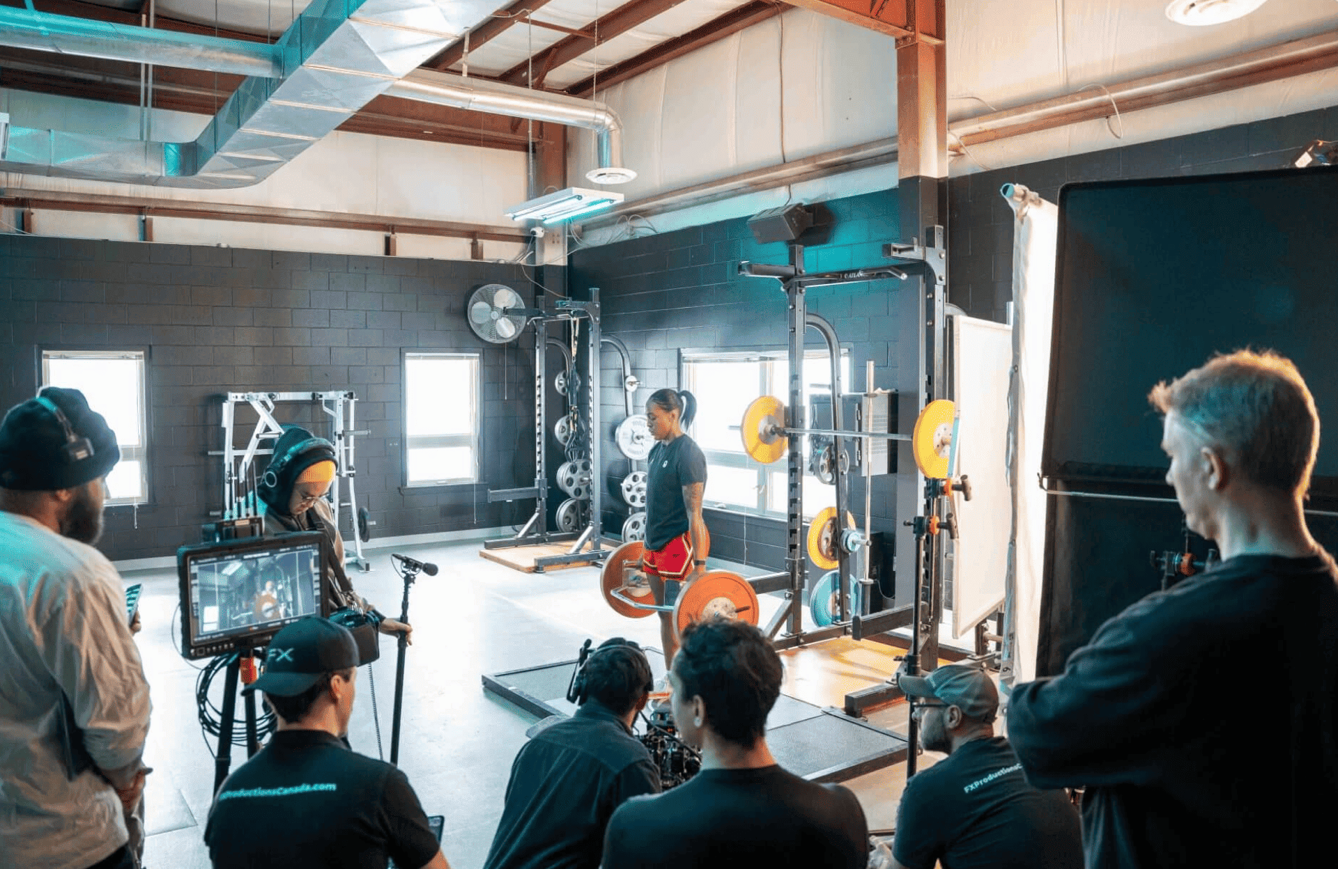 FX Productions Canada A Toronto Production Company film crew records a person lifting weights in a gym, using professional cameras and lighting equipment. Several people observe the scene. Toronto Video Production Company