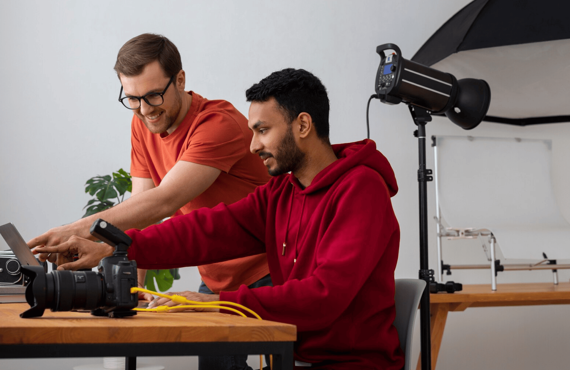 FX Productions Canada Two men in casual clothing set up camera equipment and look at a laptop in a photography studio, with lighting gear and props on wooden tables—capturing the creative energy of a Toronto Production Company. Toronto Video Production Company