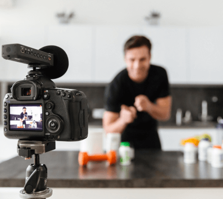 FX Productions Canada A camera on a tripod films a person behind a table with various containers and a dumbbell in a kitchen, capturing the scene for FX Productions Canada, a leading Toronto Video Production company. Toronto Video Production Company