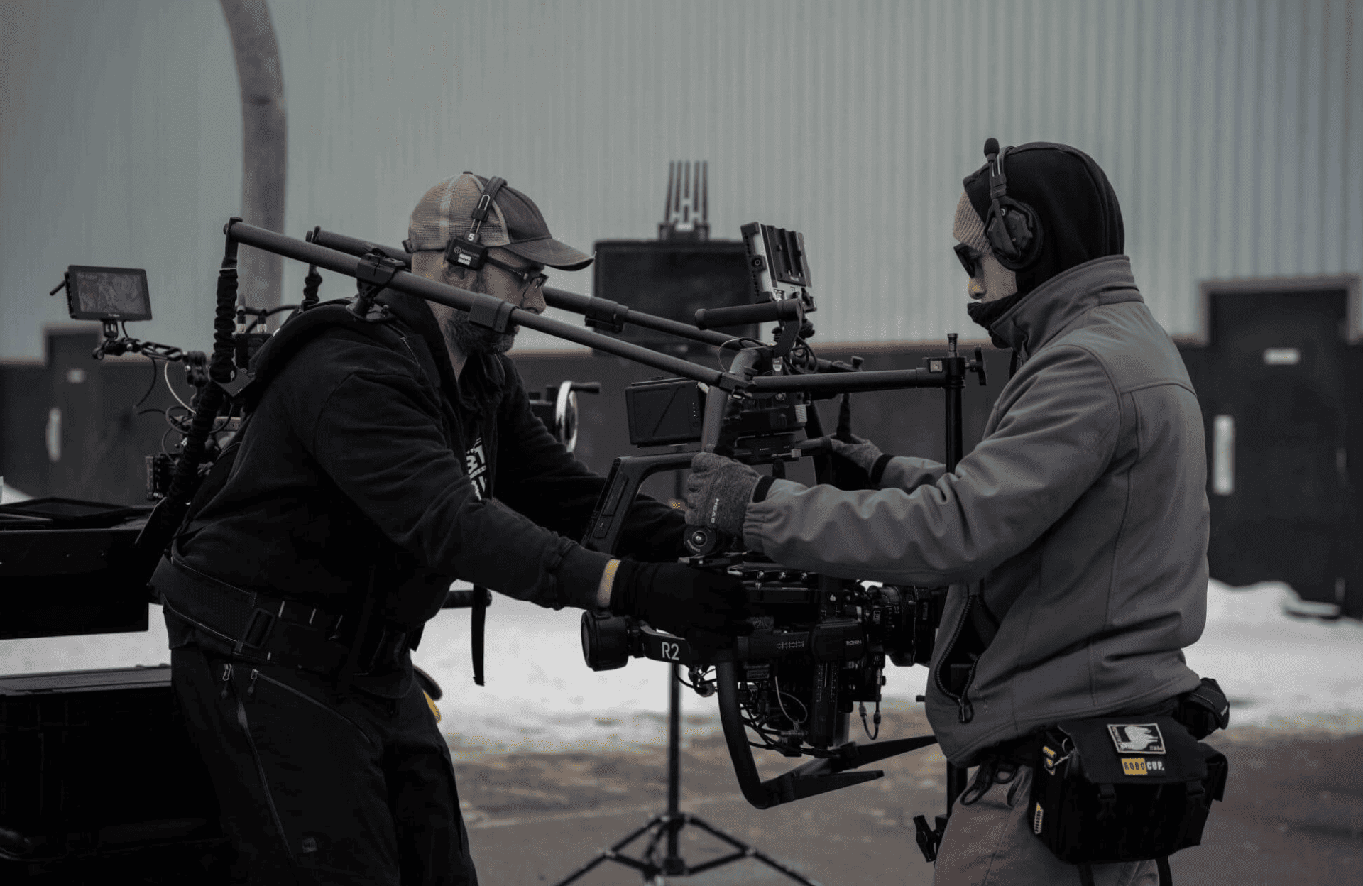 FX Productions Canada Two crew members from Toronto Production Company operate a mounted camera rig outdoors on a snowy film set, both wearing headsets and winter clothing. Snow blankets the ground in the background, capturing the essence of FX Productions Canada. Toronto Video Production Company