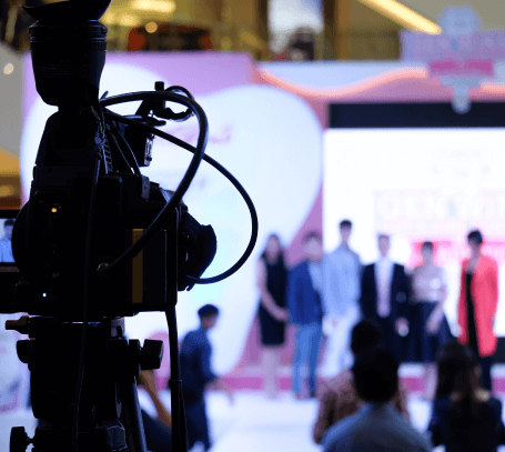 FX Productions Canada A video camera in the foreground records a group of people standing on a brightly lit stage in a blurred background, showcasing the expertise of Toronto Video Production professionals. Toronto Video Production Company