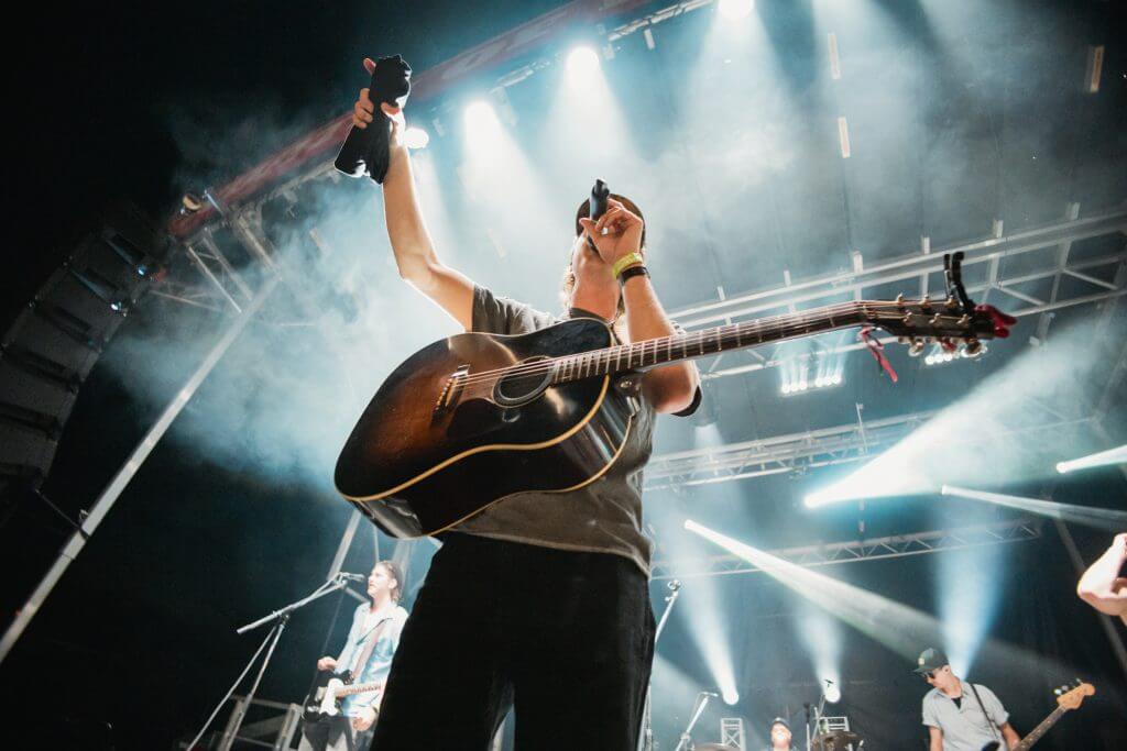 FX Productions Canada A musician with a guitar performs on stage, holding a microphone and an object in the air, with band members and stage lights in the background—captured by FX Productions Canada, a leading Toronto video production company. Toronto Video Production Company