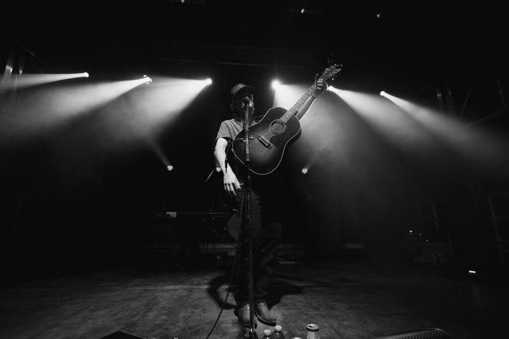 FX Productions Canada A guitarist stands on a dimly lit stage, holding an acoustic guitar upright while facing the audience, with spotlights shining in the background—captured by FX Productions Canada, a leading Video Production Company. Toronto Video Production Company