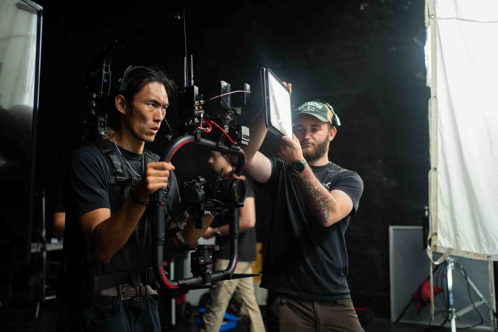 FX Productions Canada Two crew members on a film set, one operating a camera stabilizer and the other adjusting a portable LED light, showcase the expertise of FX Productions Canada, a leading Toronto Video Production company. Toronto Video Production Company