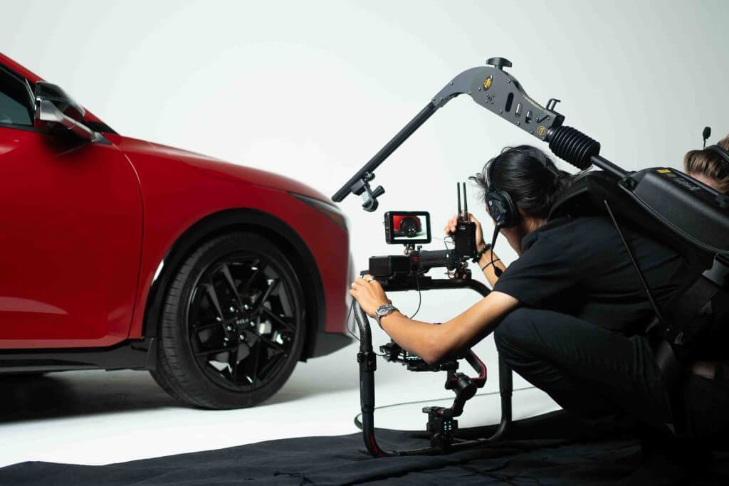 FX Productions Canada A person operates a camera rig filming the front side of a red car in a studio with a white background, showcasing the professional touch of Toronto Video Production. Toronto Video Production Company