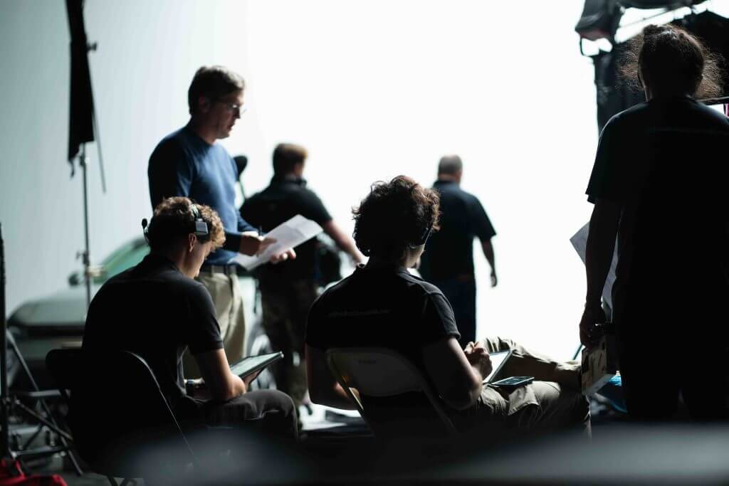 FX Productions Canada Several people are on a film set, some seated with equipment and scripts, while others stand in the background near a bright light source at FX Productions Canada, a leading Toronto Video Production company. Toronto Video Production Company