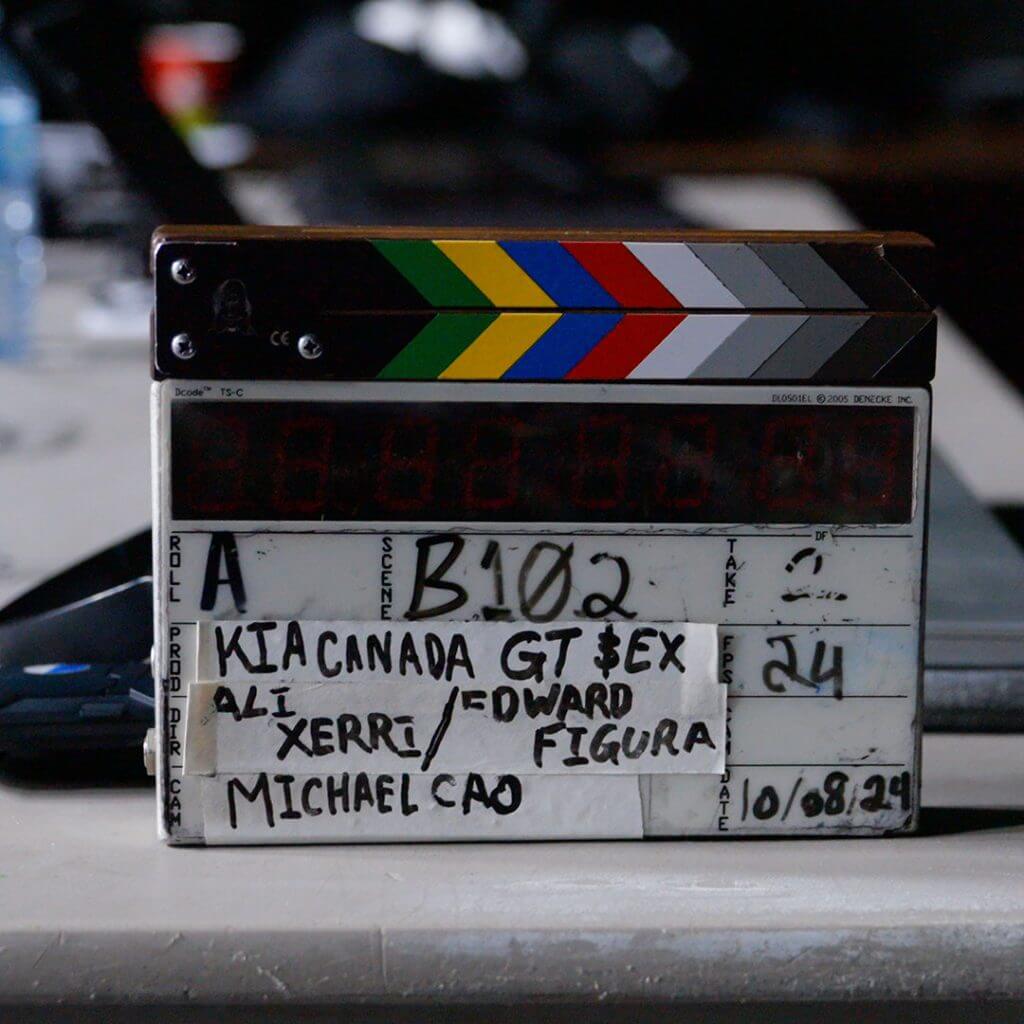 FX Productions Canada A film slate with colored stripes and handwritten text sits on a table, showing scene and take information for a production by FX Productions Canada titled "KIA CANADA GT $EX. Toronto Video Production Company