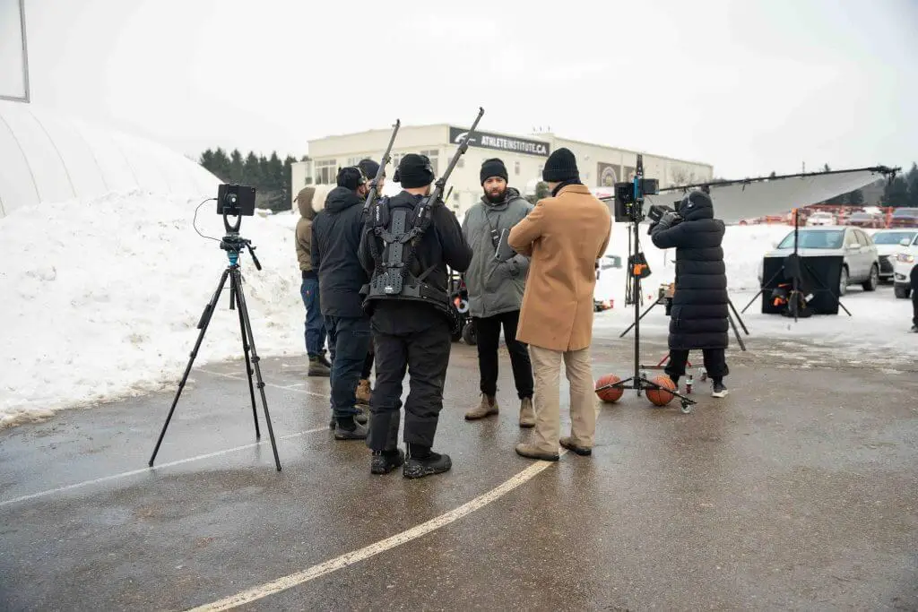 FX Productions Canada A film crew from FX Productions Canada stands outdoors on a snowy day, setting up equipment and having a discussion in a parking lot with snowbanks in the background. Toronto Video Production Company