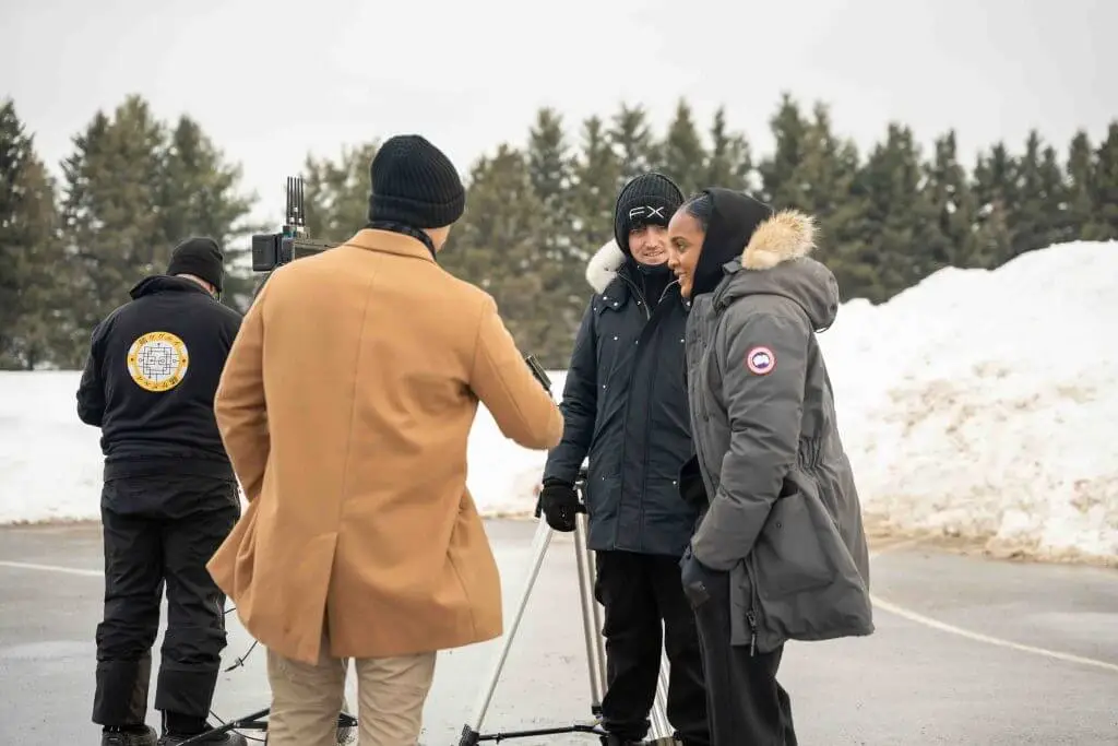 FX Productions Canada Four people stand outdoors in winter clothing near a camera on a tripod, with snowbanks and trees visible in the background—an authentic behind-the-scenes moment from a Toronto Video Production team at work. Toronto Video Production Company