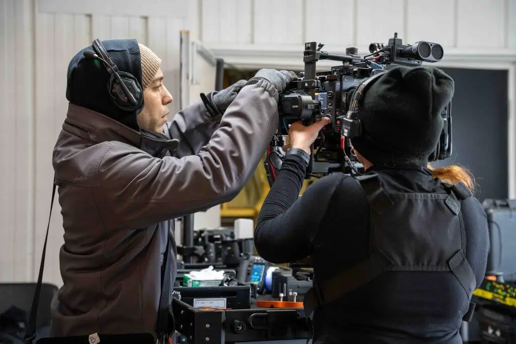 FX Productions Canada Two crew members wearing headsets and winter clothing adjust a professional video camera on set in an indoor setting, showcasing the expertise of FX Productions Canada, a leading Toronto Video Production company. Toronto Video Production Company