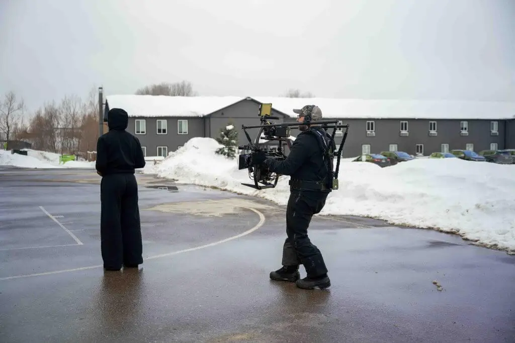 FX Productions Canada A person in black stands on a wet outdoor basketball court in winter as a cameraman from FX Productions Canada films with a shoulder-mounted rig; snow piles are in the background. Toronto Video Production Company