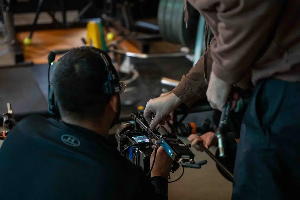 FX Productions Canada Two people wearing headsets adjust settings on a professional video camera in a gym, showcasing Toronto Video Production expertise by FX Productions Canada, with gym equipment visible in the background. Toronto Video Production Company