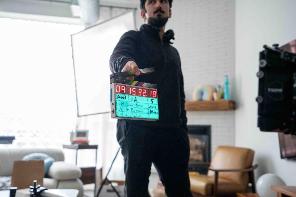 FX Productions Canada A person holds a film clapperboard in front of a camera on a movie set, with living room furniture and filmmaking equipment visible in the background—just another creative day at FX Productions Canada. Toronto Video Production Company