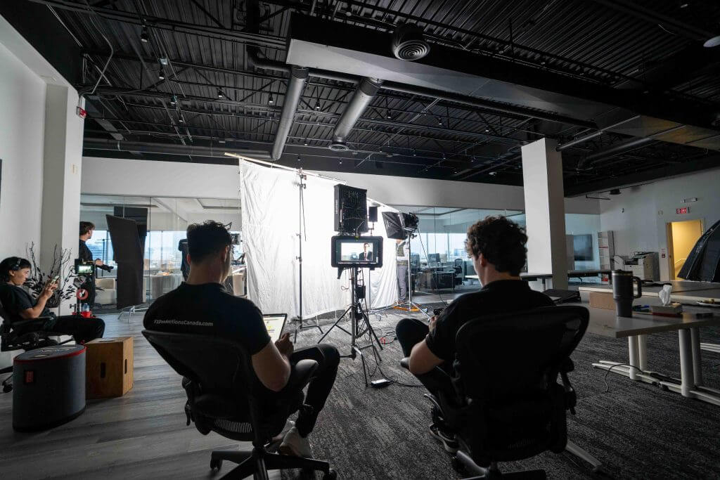 FX Productions Canada People are seated and working on equipment in a modern office space set up with cameras, lights, and a large white backdrop for a Toronto Video Production or photo shoot by FX Productions Canada. Toronto Video Production Company
