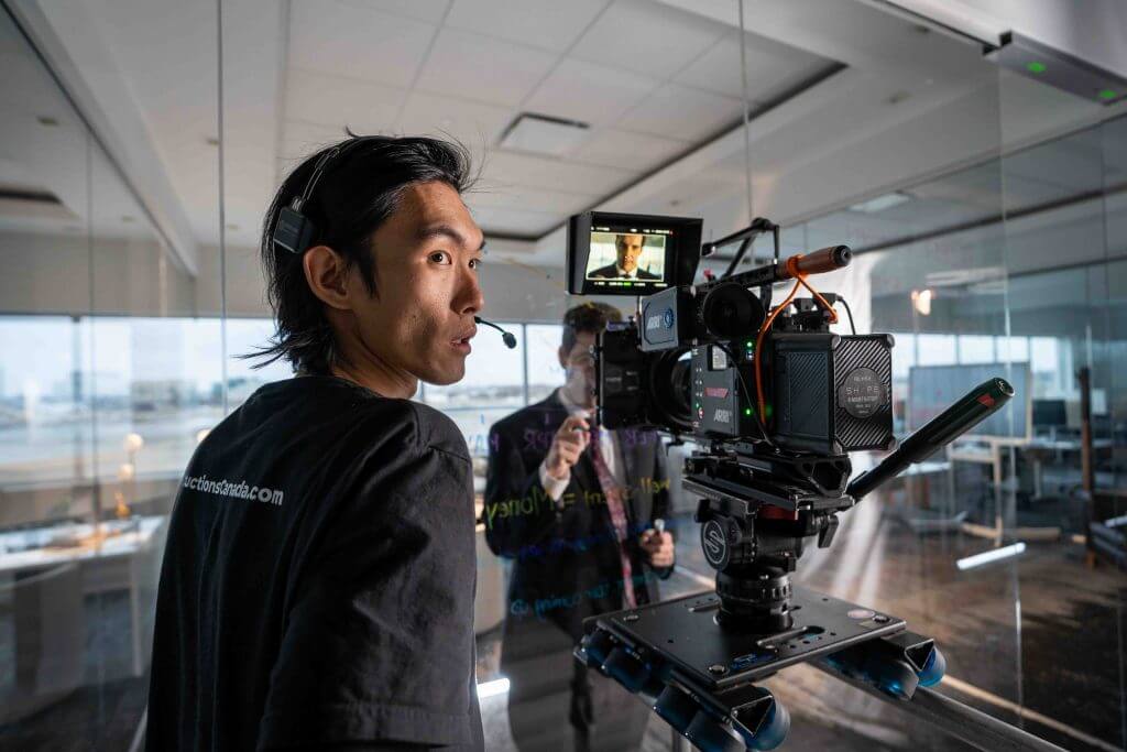 FX Productions Canada A person wearing a headset operates a professional camera on a dolly in an office, filming someone writing on a glass wall—showcasing the expertise of FX Productions Canada, a leading Toronto Video Production company. Toronto Video Production Company