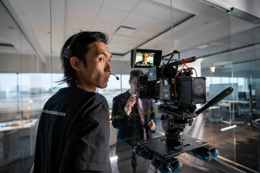 FX Productions Canada A person wearing a headset operates a professional camera on a dolly in an office, filming someone writing on a glass wall—showcasing the expertise of FX Productions Canada, a leading Toronto Video Production company. Toronto Video Production Company