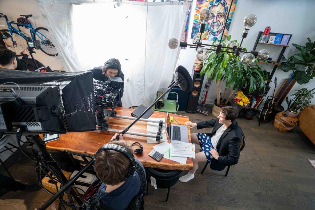 FX Productions Canada A Toronto Video Production crew records a person working at a desk with a laptop in a brightly lit room decorated with plants, bicycles, guitars, and artwork. Toronto Video Production Company