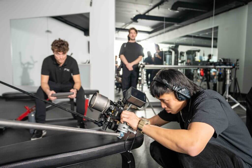 FX Productions Canada A person operates a professional video camera with headphones on, while another sits with a tablet and a third stands in the background—capturing the energy of a Toronto Production Company in a dynamic studio setting. Toronto Video Production Company