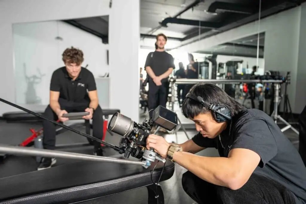 FX Productions Canada A person operates a professional video camera with headphones on, while another sits with a tablet and a third stands in the background—capturing the energy of a Toronto Production Company in a dynamic studio setting. Toronto Video Production Company