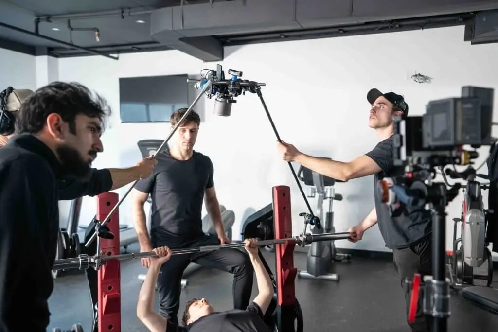 FX Productions Canada A film crew from FX Productions Canada records a person bench pressing weights in a gym, with one team member holding a boom microphone and another operating the camera. Toronto Video Production Company
