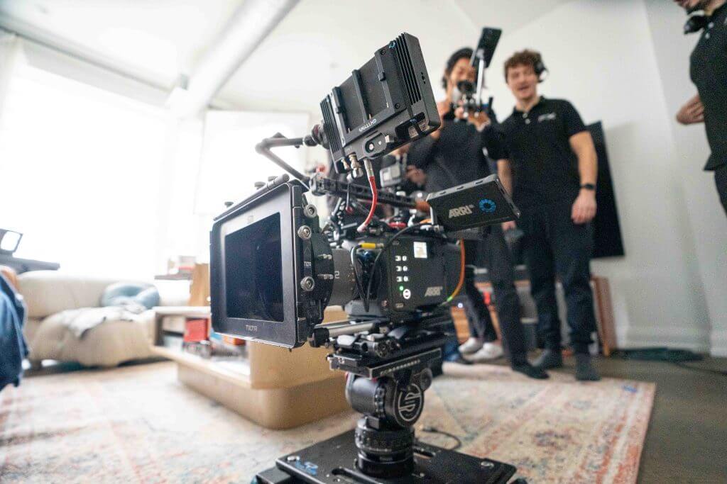 FX Productions Canada A professional video camera setup by FX Productions Canada is positioned in the foreground of a living room, with three crew members standing and talking in the background, showcasing the expertise of a leading Toronto Video Production company. Toronto Video Production Company