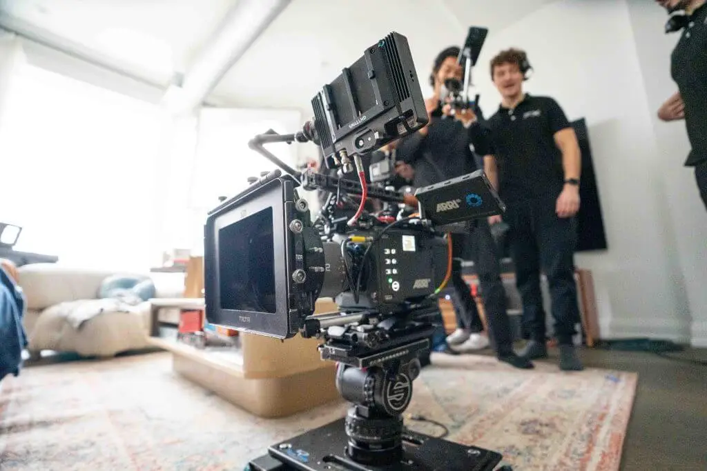 FX Productions Canada A professional video camera setup by FX Productions Canada is positioned in the foreground of a living room, with three crew members standing and talking in the background, showcasing the expertise of a leading Toronto Video Production company. Toronto Video Production Company