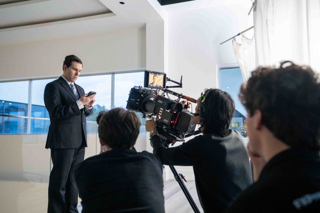 FX Productions Canada A Toronto Production Company film crew records a man in a suit speaking into his phone, using a professional camera setup in a brightly lit indoor space. Toronto Video Production Company