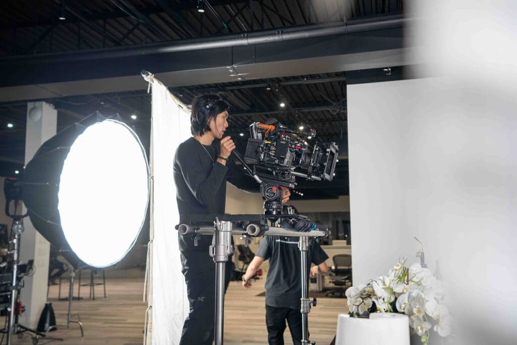 FX Productions Canada A person operating a professional video camera on a tripod in a studio with lighting equipment and white backdrop, showcasing the expertise of Toronto Production Company in high-quality video production. Toronto Video Production Company