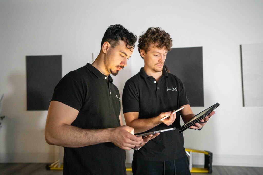 FX Productions Canada Two men in black polo shirts reviewing and discussing information on tablets in a modern, minimalistic office setting at a Toronto Production Company. Toronto Video Production Company