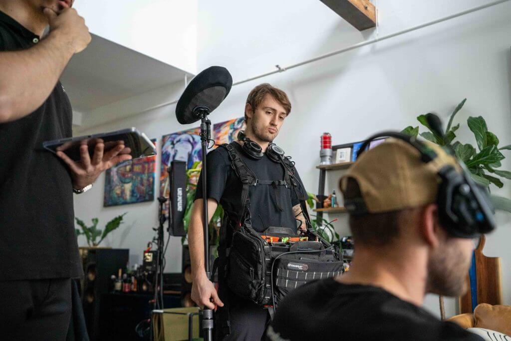 FX Productions Canada A sound technician wearing headphones and carrying audio equipment stands indoors at FX Productions Canada, while two other people with headsets work nearby for this Toronto Video Production. Toronto Video Production Company
