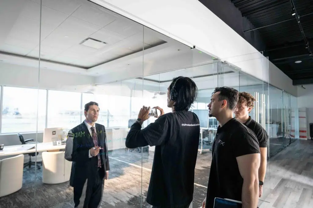 FX Productions Canada A man in a suit stands in a modern office while three casually dressed men face him, one holding a phone as if recording—a scene that captures the energy of a Toronto Video Production team at work. Toronto Video Production Company