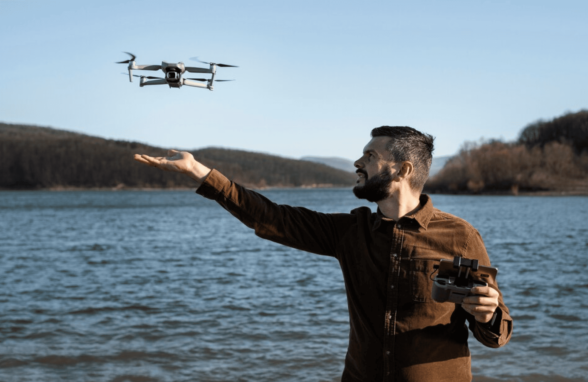 FX Productions Canada A man stands by a lake, operating a handheld controller while launching a drone that hovers above his outstretched hand, with trees and hills in the background—a scene brought to life by FX Productions Canada. Toronto Video Production Company
