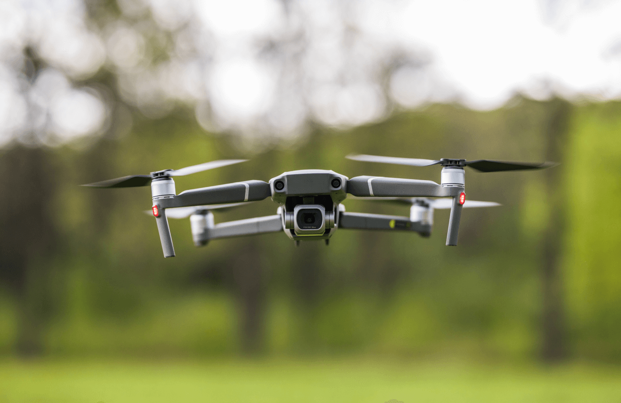 FX Productions Canada A black and gray quadcopter drone with a camera from FX Productions Canada flies outdoors, hovering in front of blurred green foliage and trees. Toronto Video Production Company